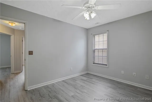 an empty room with wooden floor chandelier fan and windows