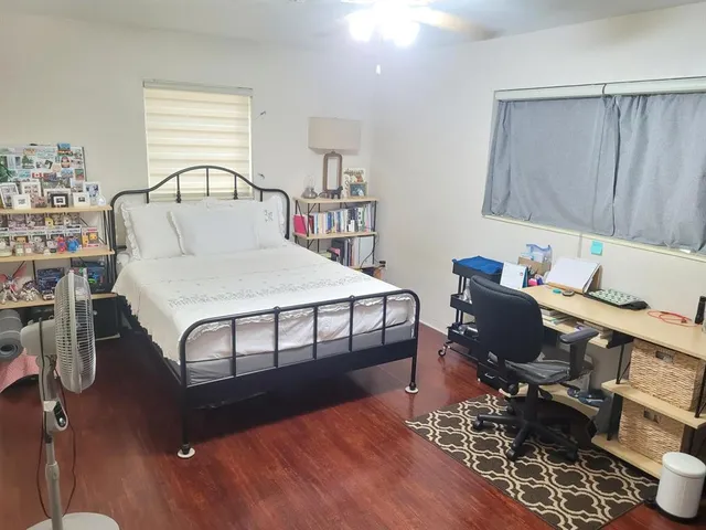 a bedroom with a bed a desk and chair with the wooden floor