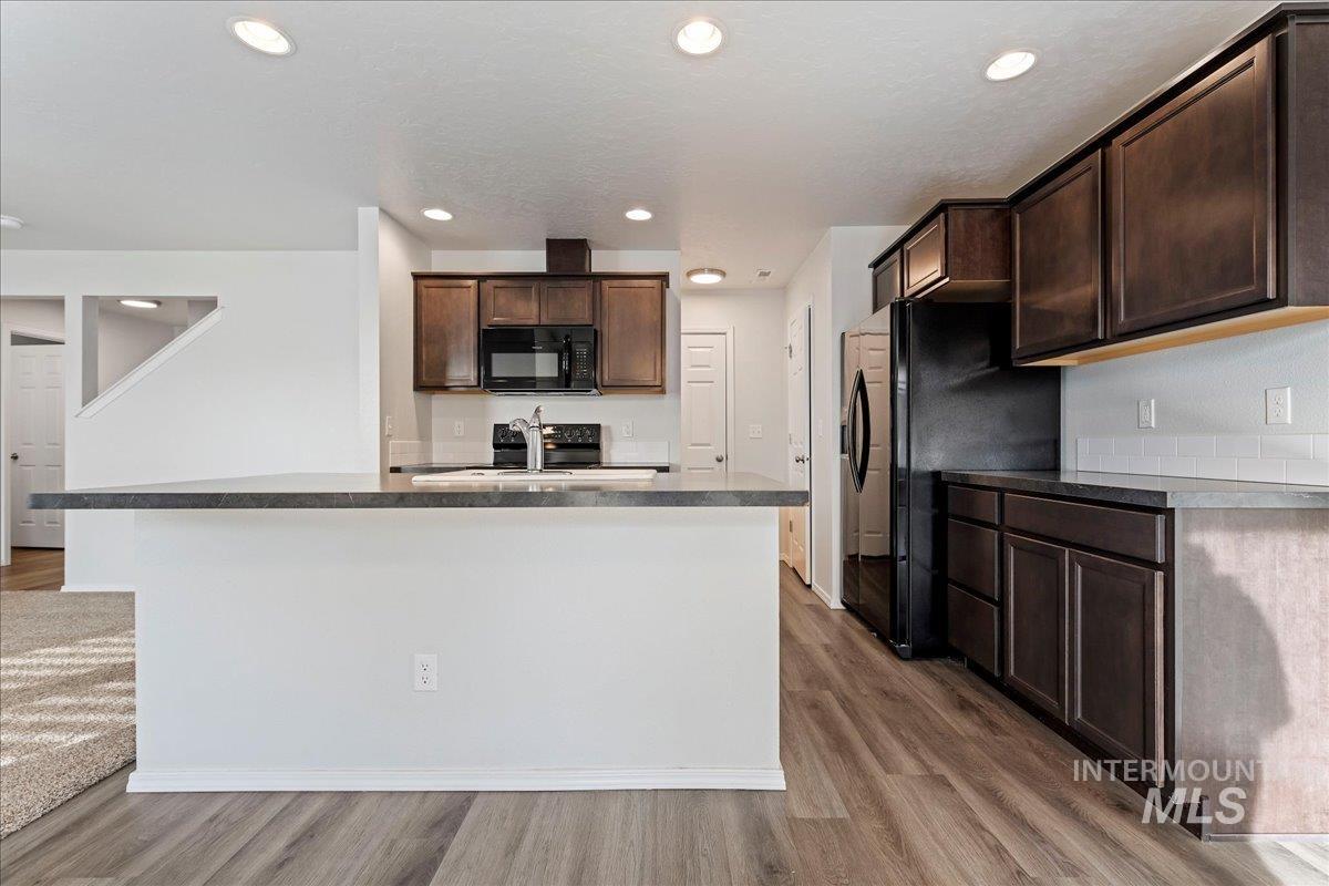 961 West Apple Pine Street Meridian, ID 83646 - Photo 5 of 30 Kitchen featuring dark brown cabinetry, dark countertops, light wood-style flooring, a center island with sink, and recessed lighting