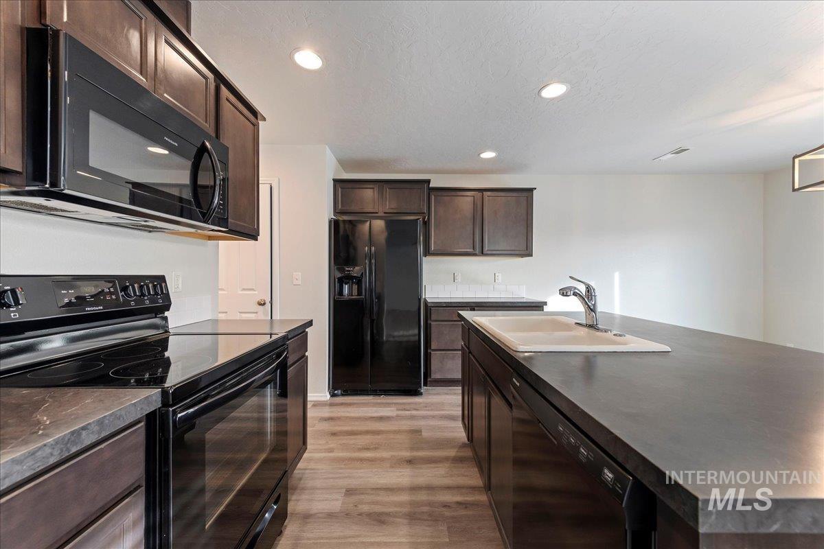 961 West Apple Pine Street Meridian, ID 83646 - Photo 7 of 30 Kitchen featuring black appliances, dark brown cabinetry, recessed lighting, a kitchen island with sink, and light wood finished floors