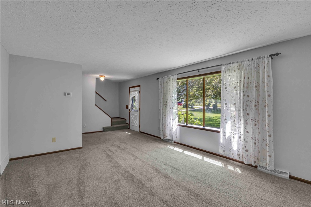 6635 Taylor Road Painesville, OH 44077 - Photo 26 of 41 Carpeted living area featuring a large picture window, a front entry door with decorative glass, and a visible staircase with carpeted treads