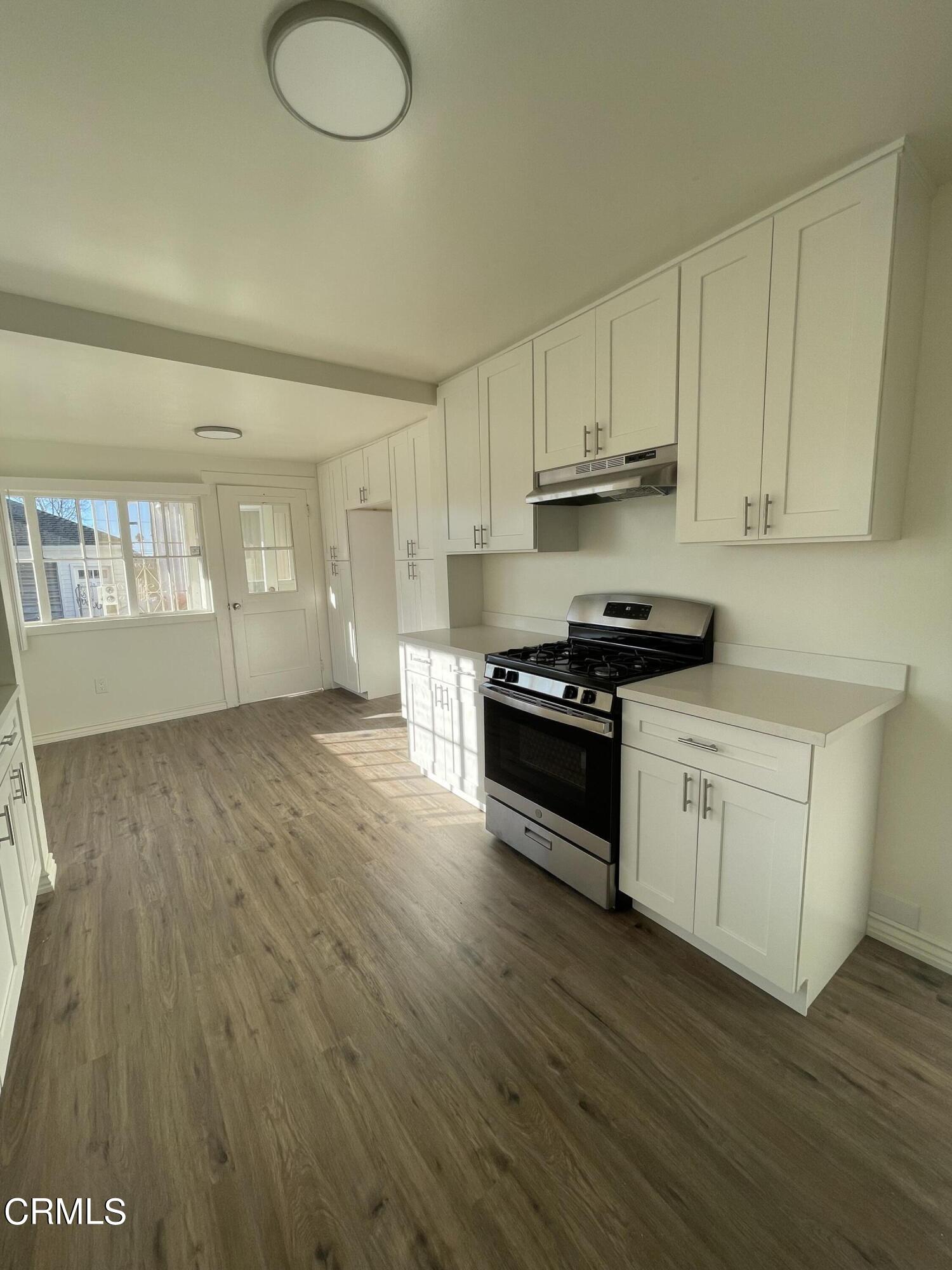 218 Wolff Street Oxnard, CA 93033 - Photo 4 of 12 a kitchen with granite countertop a stove a sink and white cabinets with wooden floor