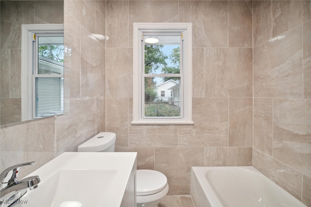 8796 West Ridgewood Drive Cleveland, OH 44130 - Photo 24 of 38 Bathroom featuring tile walls, a bathing tub, and toilet