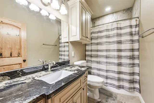 a bathroom with a granite countertop bathtub sink vanity mirror and toilet