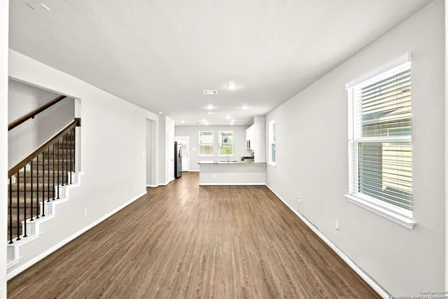a view of an empty room with kitchen and window