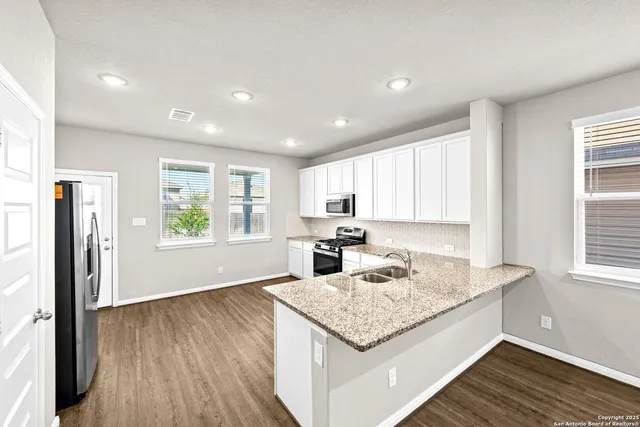 a kitchen with stainless steel appliances a sink dishwasher stove and white cabinets with wooden floor