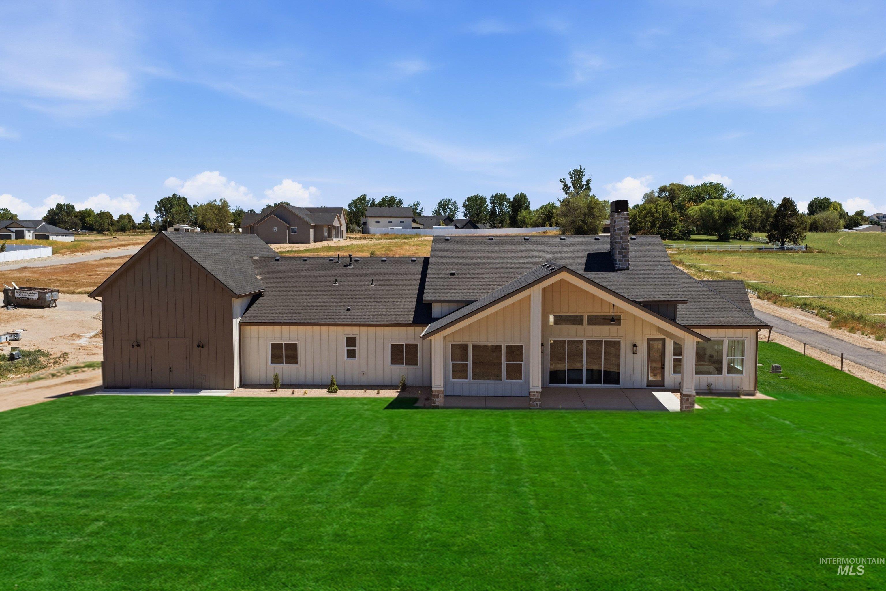 24763 Ardmore Court Caldwell, ID 83607 - Photo 48 of 50 Expansive green lawn with a newly constructed dwelling featuring a covered patio, large sliding glass doors, a prominent stone chimney, and a separate attached outbuilding with barn doors