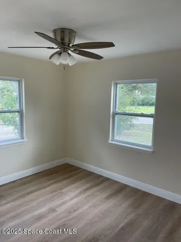 an empty room with wooden floor fan and windows