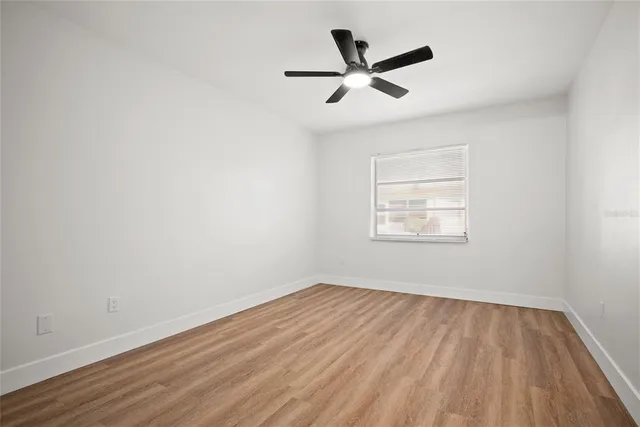 an empty room with wooden floor ceiling fan and windows