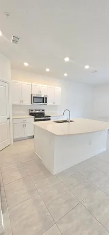 a large white kitchen with kitchen island a sink stainless steel appliances and cabinets
