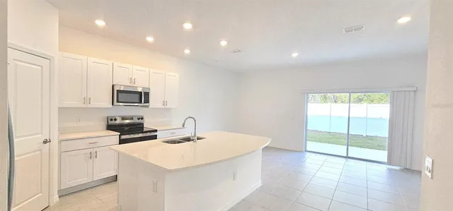 a kitchen with stainless steel appliances a sink a stove a microwave a refrigerator a white cabinets and a window