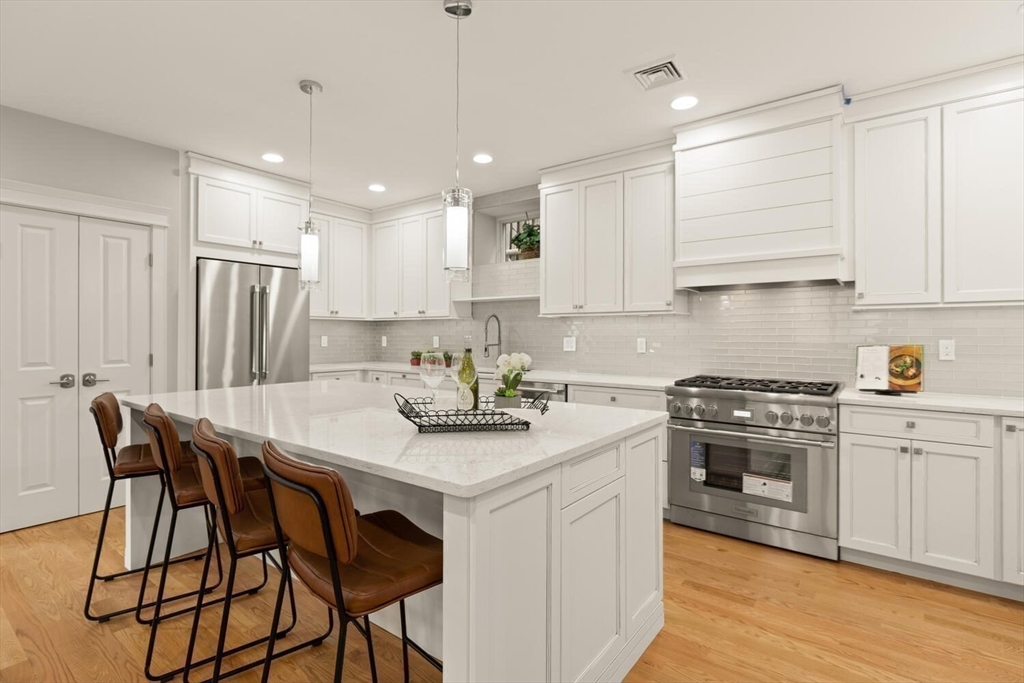 7 Whitman Street, Unit 1 Somerville, MA 02144 - Photo 10 of 35 a kitchen with stainless steel appliances kitchen island granite countertop a stove a sink a refrigerator and white cabinets with wooden floor