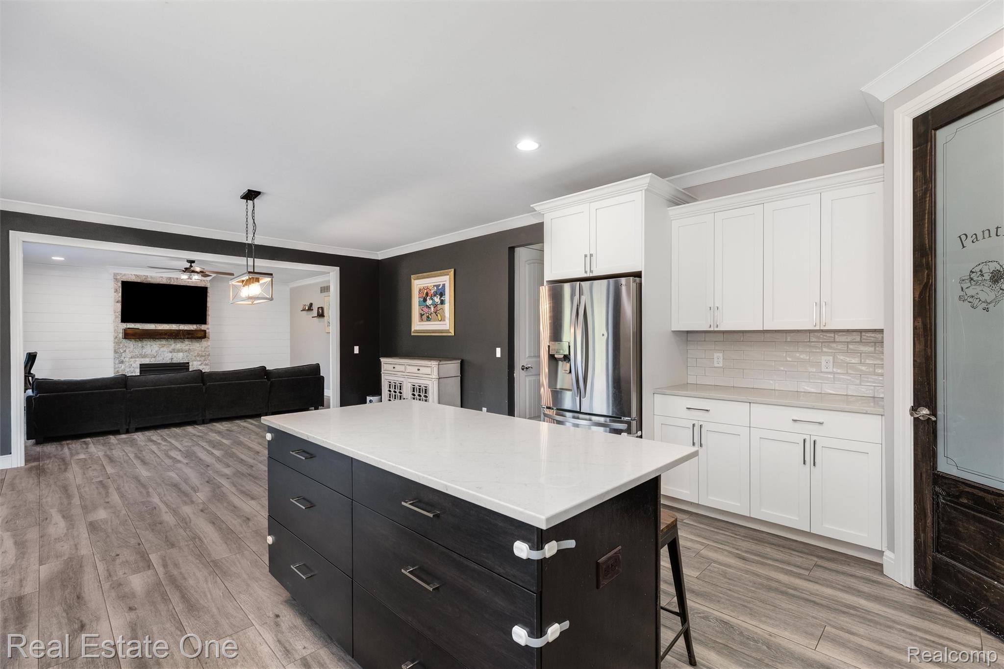 2983 28 Mile Road Washington, MI 48094 - Photo 11 of 54 Spacious kitchen featuring a central island with a light-toned countertop and dark wood-finish cabinetry, stainless steel refrigerator, white upper and lower cabinetry, white subway tile backsplash, and wood-finish flooring