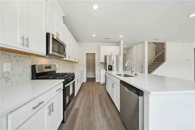 a kitchen with stainless steel appliances granite countertop a stove a sink and white cabinets with wooden floor next to windows