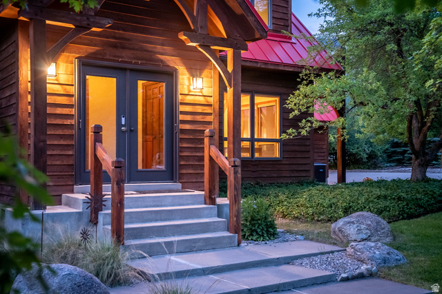 435 Canyon Road Millville, UT 84326 - Photo 91 of 113 Timber-frame entrance featuring double glass doors, a red metal roof, concrete steps, wood railings, and exterior wall sconces