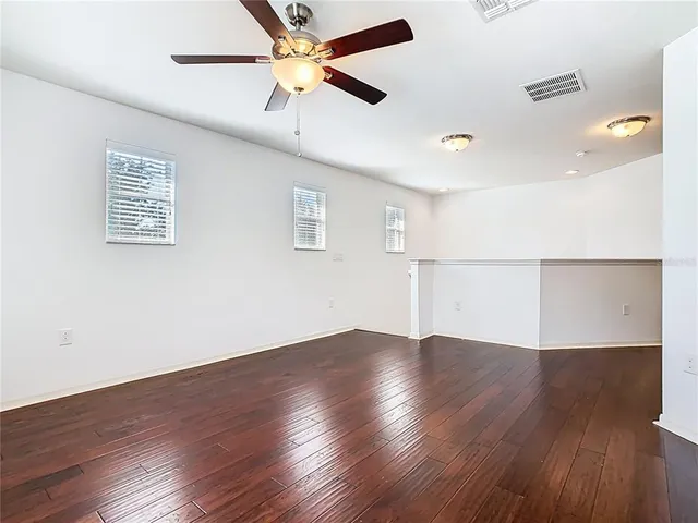 an empty room with wooden floor chandelier fan and windows