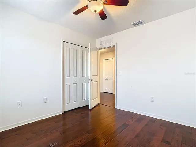 an empty room with wooden floor fan and windows
