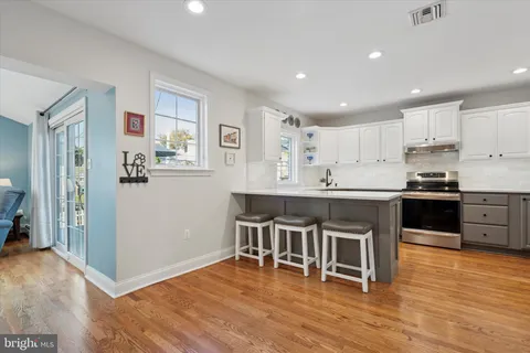 a kitchen with stainless steel appliances kitchen island granite countertop a stove a refrigerator a sink a dining table and chairs with wooden floor