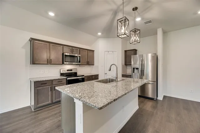a large kitchen with granite countertop a sink a counter space stainless steel appliances and cabinets