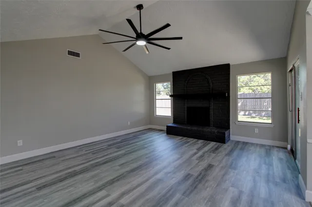 an empty room with wooden floor a ceiling fan and windows