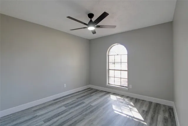 an empty room with wooden floor fan and windows