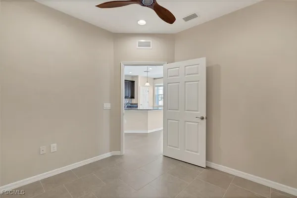 an empty room with chandelier fan and kitchen view