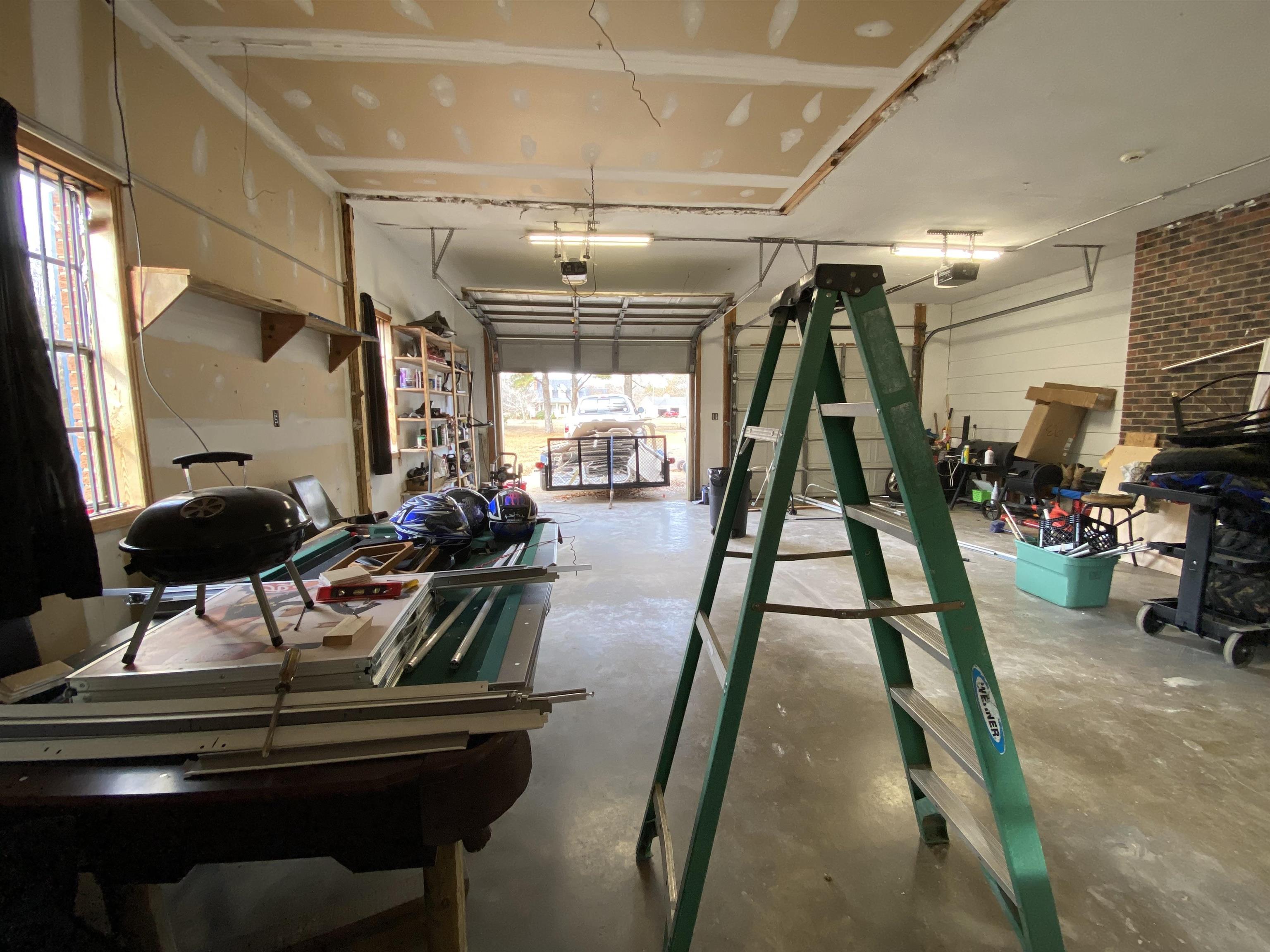 329 Mayflower Road Ramer, TN 38367 - Photo 19 of 20 Expansive multi-purpose space featuring a roll-up garage door, exposed brick accent wall, high ceilings, and multiple windows for natural light