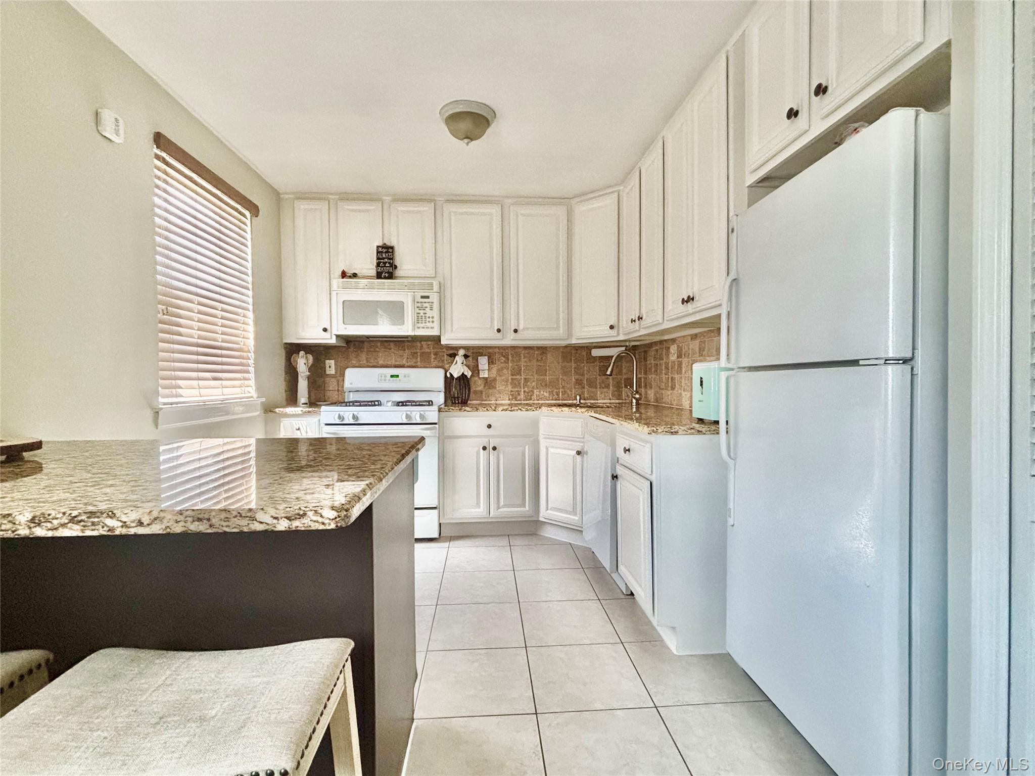 72-29 Little Neck Parkway, Unit 2 Queens, NY 11426 - Photo 9 of 24 a kitchen with granite countertop a refrigerator sink stove and white cabinets