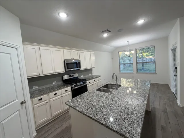 a large kitchen with stainless steel appliances granite countertop a stove a sink dishwasher and a refrigerator with wooden floor