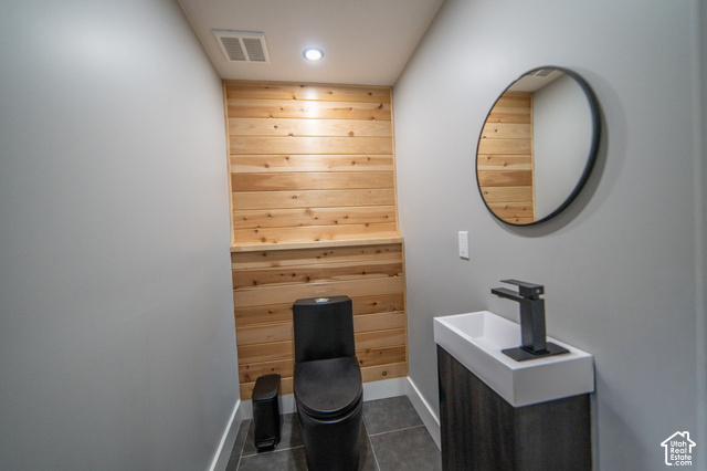 7676 Jefferson Road Magna, UT 84044 - Photo 18 of 24 Wood panel accent wall, dark gray floor tiling, circular wall mirror, wall-mounted sink with dark finish faucet, dark finish toilet