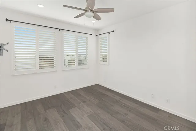 an empty room with wooden floor fan and windows