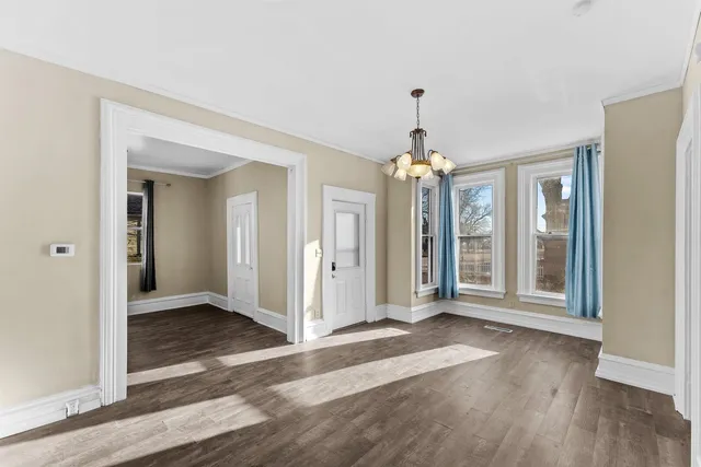 an empty room with wooden floor chandelier and windows