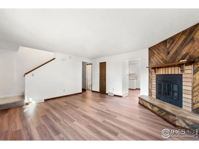 a view of an empty room with wooden floor fireplace and a window