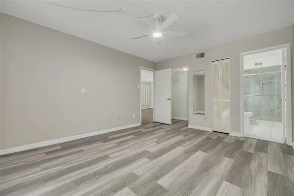 a view of an empty room with wooden floor and a ceiling fan