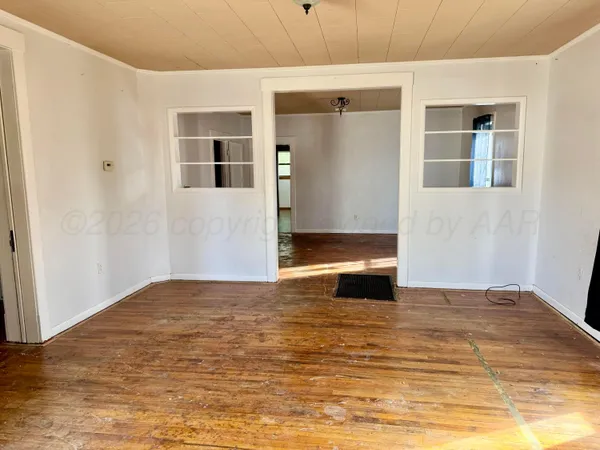 a view of an empty room with wooden floor and a kitchen