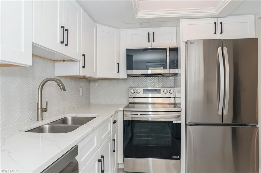 1155 Sandpiper Street, Unit B3 Naples, FL 34102 - Photo 4 of 21 Kitchen featuring stainless steel appliances, light stone counters, white cabinetry, decorative backsplash, and ornamental molding