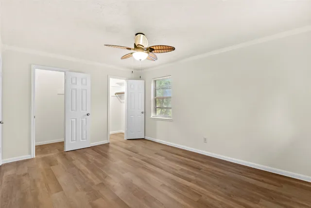 an empty room with wooden floor ceiling fan and windows