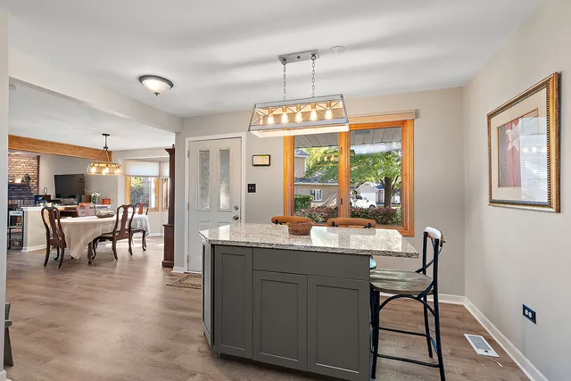 a dining hall with stainless steel appliances granite countertop a stove a sink a dining table and chairs with wooden floor