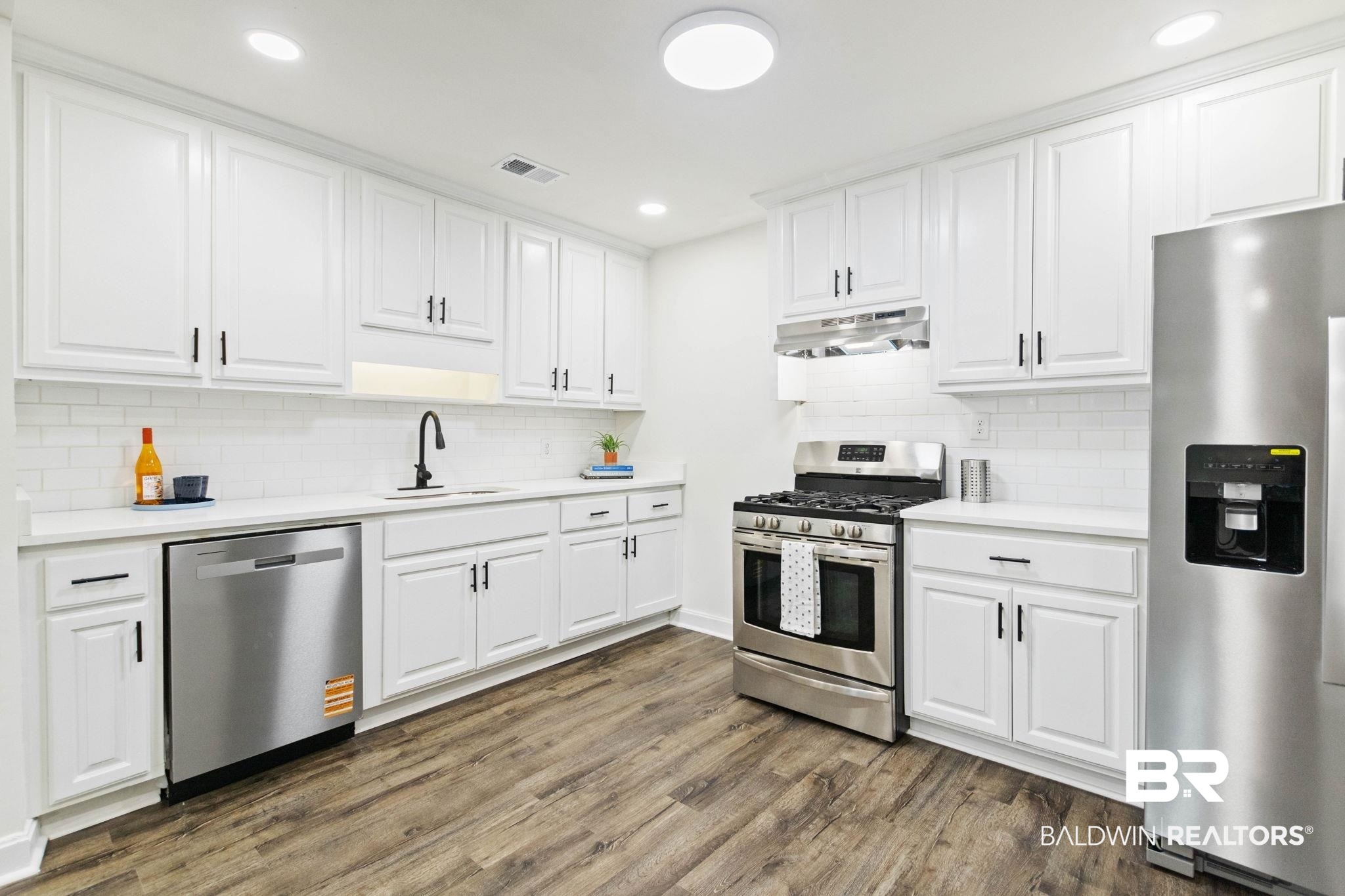 618 Pine Street Saraland, AL 36571 - Photo 17 of 41 Kitchen with appliances with stainless steel finishes, white cabinetry, dark wood-style flooring, tasteful backsplash, and recessed lighting