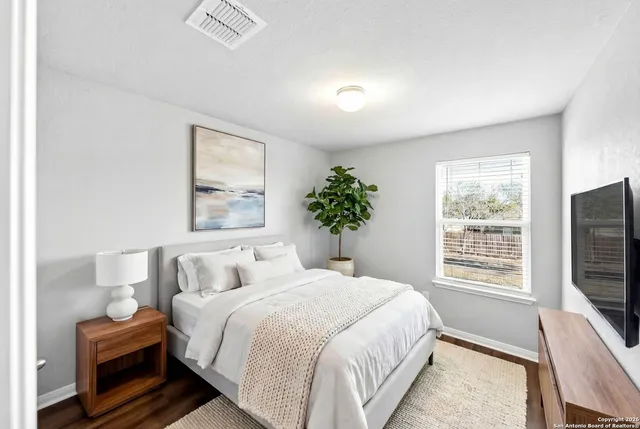 a bedroom with bed a flat tv screen and a potted plant