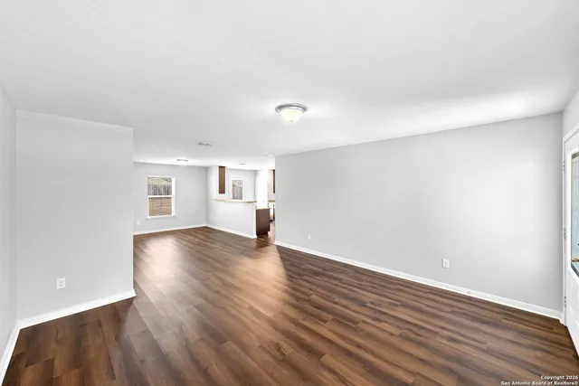 a view of empty room with wooden floor and kitchen