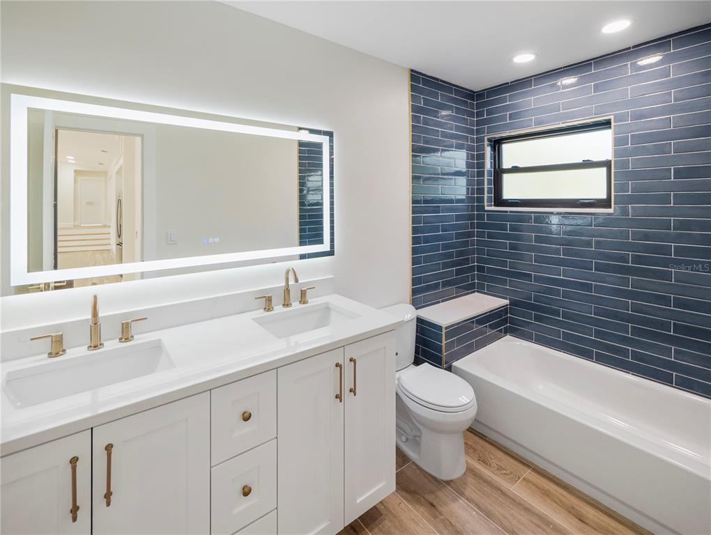 6790 Edgeworth Drive Orlando, FL 32819 - Photo 34 of 57 a bathroom with a granite countertop toilet a sink a mirror a bathtub and shower