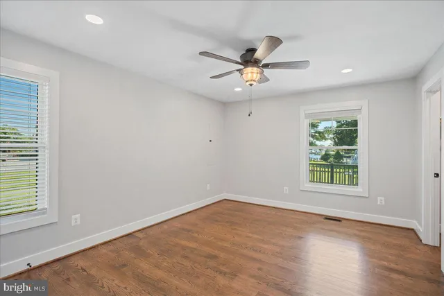 an empty room with wooden floor fan and windows