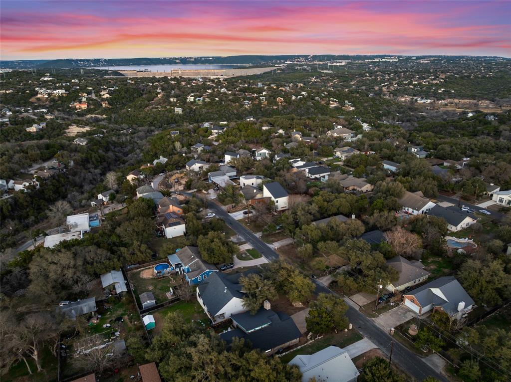 2210 Red Fox Road Austin, TX 78734 - Photo 36 of 40 An aerial perspective reveals a tree-filled neighborhood with a distant dam and lake under a dramatic sky.