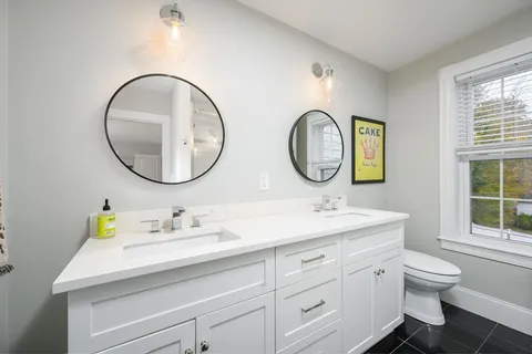a bathroom with a toilet a double vanity sink and a mirror