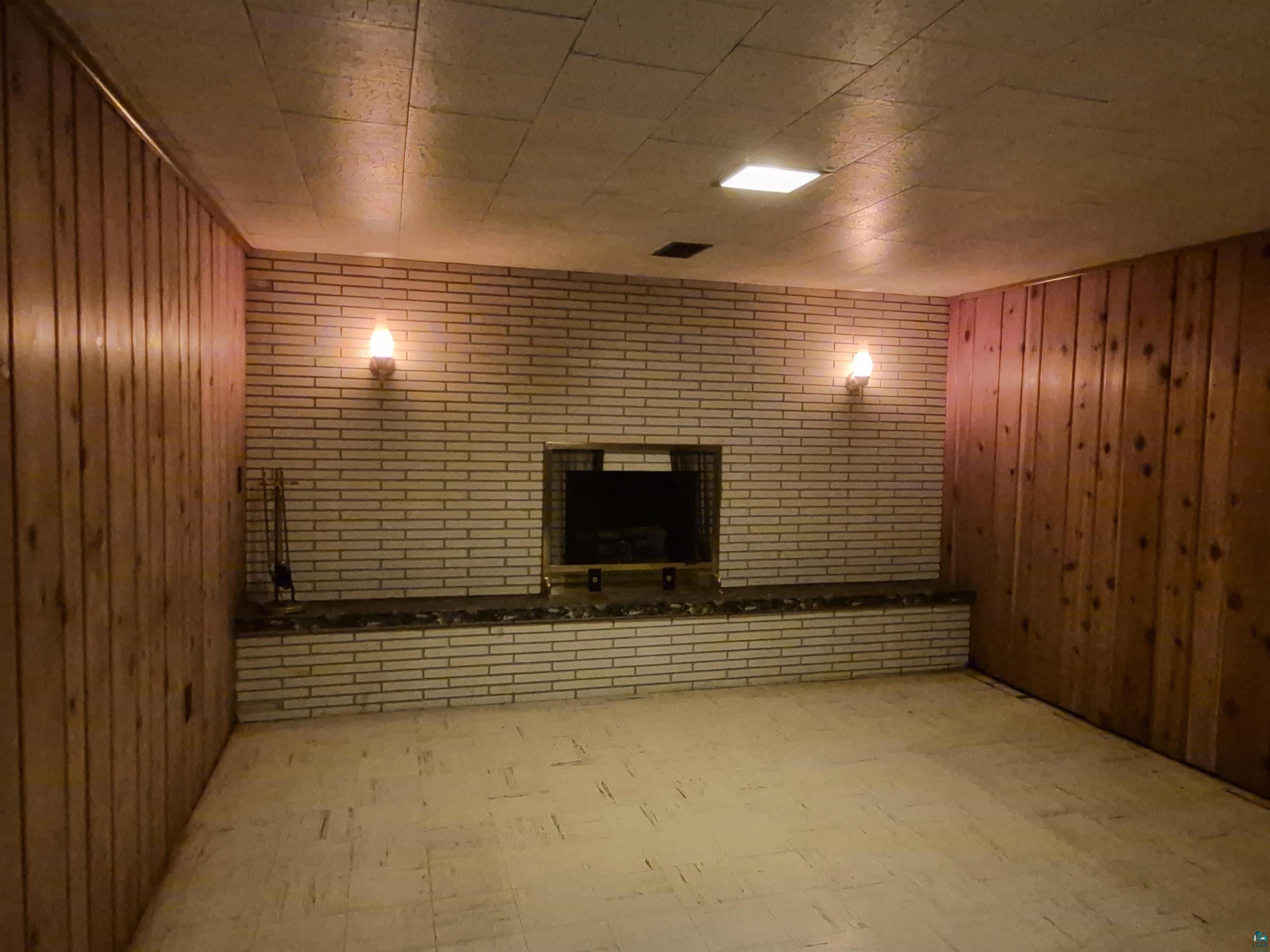 2109 West 22nd Street Duluth, MN 55811 - Photo 29 of 29 Brick fireplace with hearth, flanked by wood paneling and sconce lighting