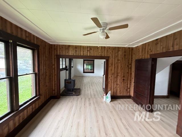 204 Front Street Kooskia, ID 83539 - Photo 13 of 25 Unfurnished living room with wooden walls, a ceiling fan, a wood stove, light wood-style floors, and ornamental molding