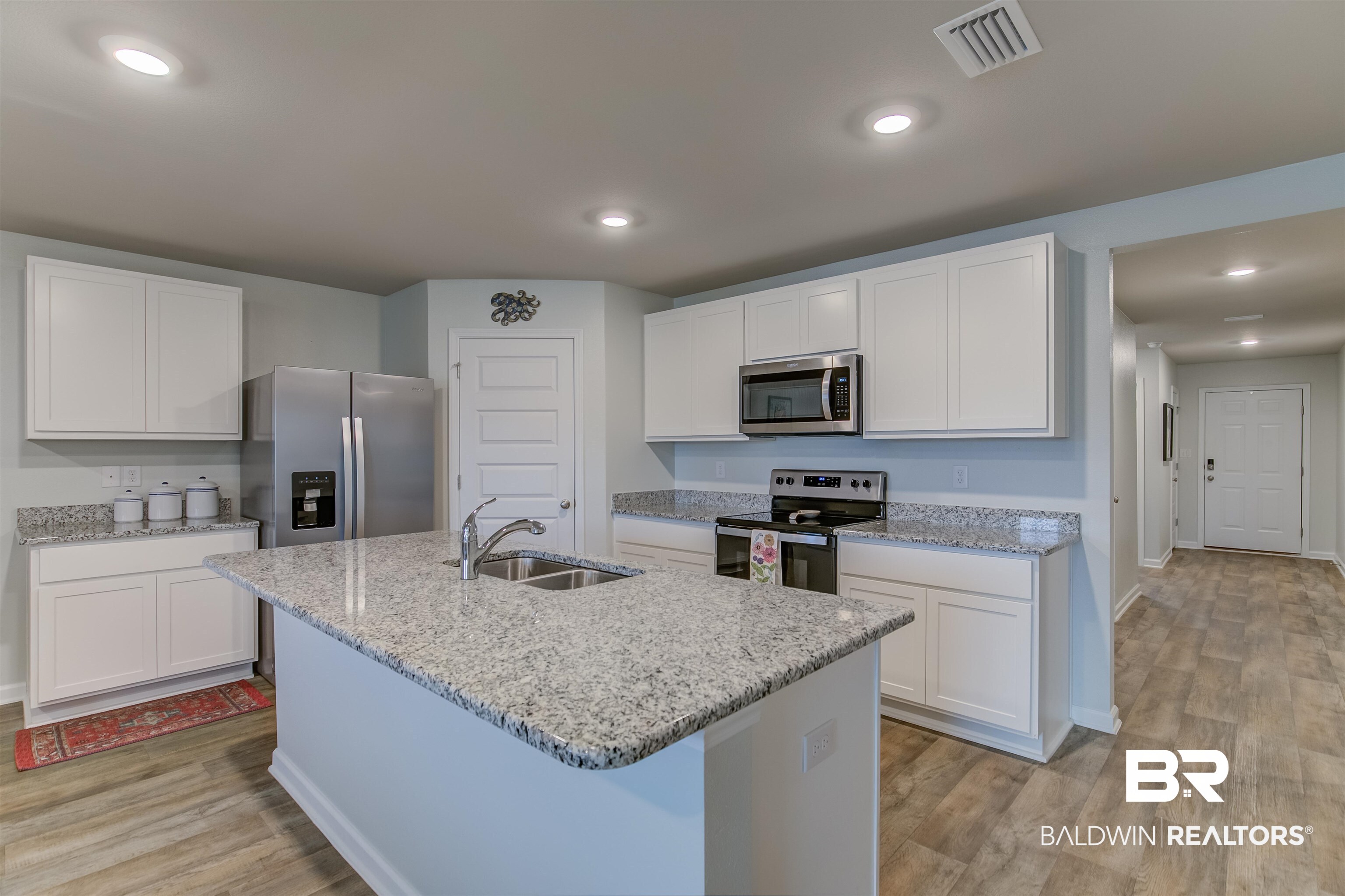 8033 Irwin Loop Daphne, AL 36526 - Photo 17 of 38 Kitchen featuring an island with double basin sink, white cabinetry, integrated stainless steel appliances, and wood-finish flooring