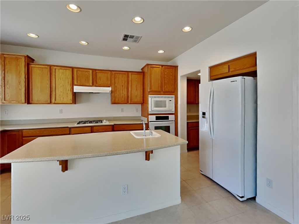 9456 Bluff Ledge Avenue Las Vegas, NV 89149 - Photo 24 of 35 Kitchen with recessed lighting, white appliances, a center island with sink, a breakfast bar area, and light tile patterned flooring