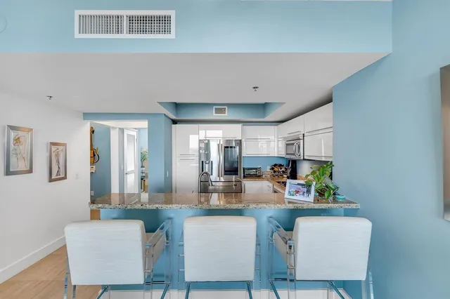 a kitchen with stainless steel appliances kitchen island granite countertop a dining table chairs and a refrigerator